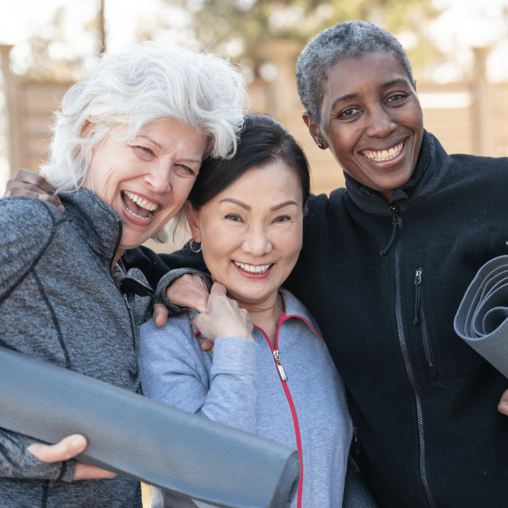 Three older women are smiling while holding yoga mats.