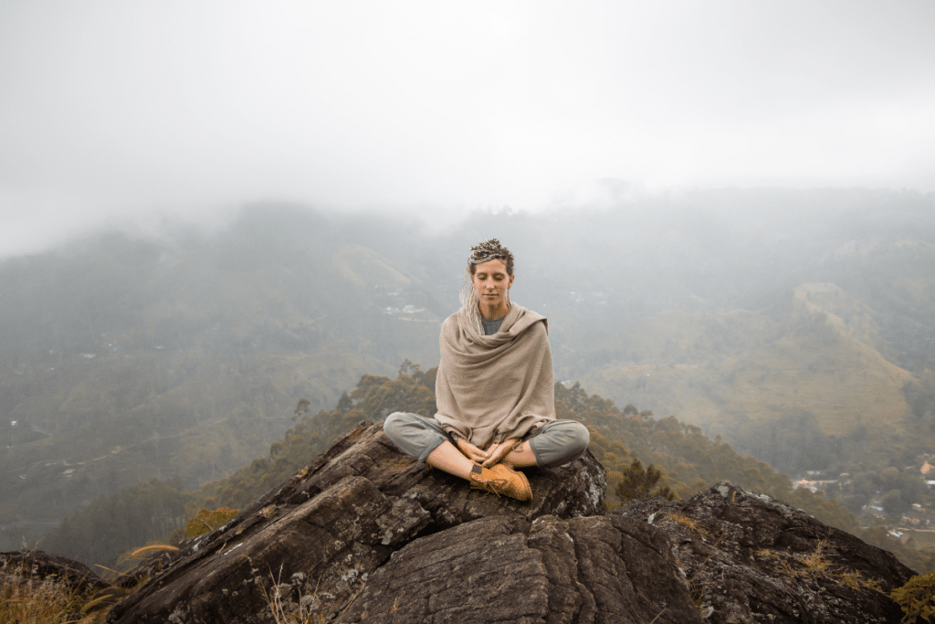 Woman meditating on top of a mountain.
