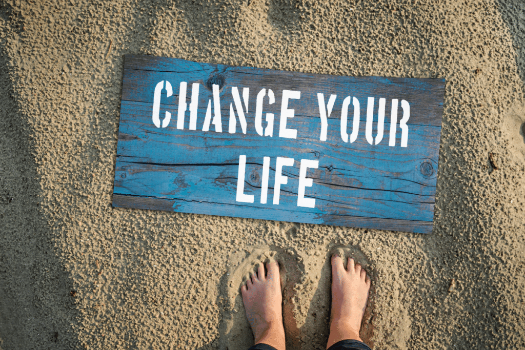 A person's feet standing in the sand next to a sign that says change your life.
