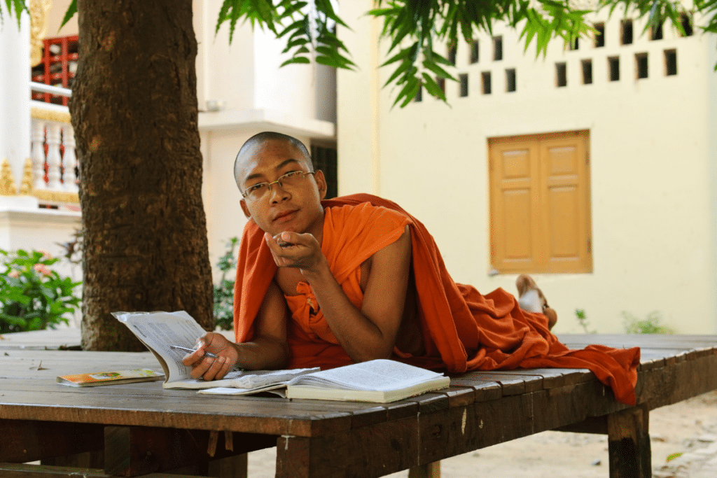 A monk laying on a table reading a book.