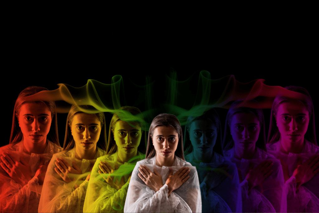 A woman with an aura in a rainbow robe is standing in front of a black background.