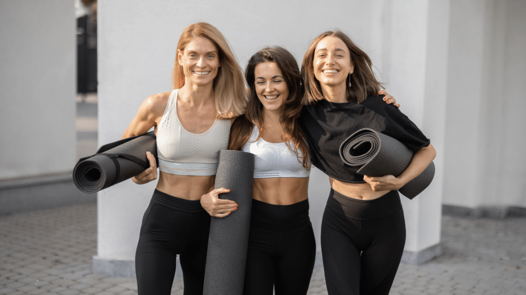 Three women holding yoga mats in front of a building.