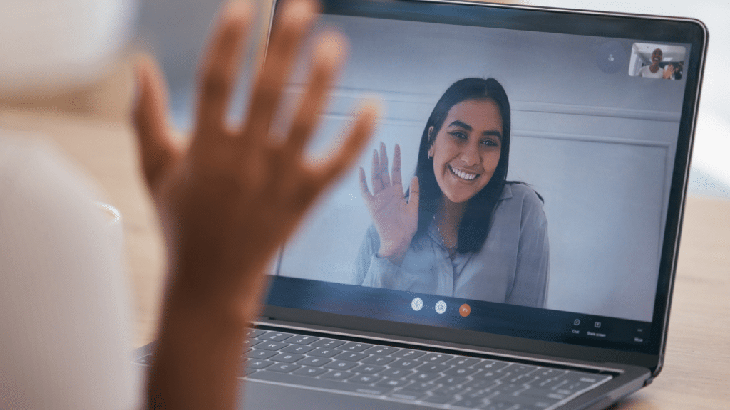 A woman on a laptop with her hand up on a video call.