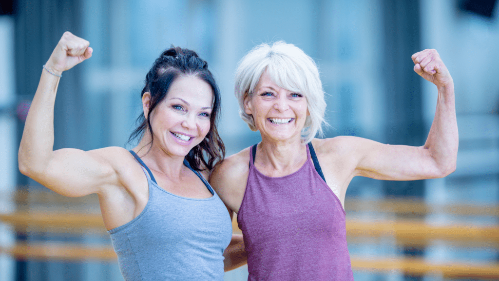 Two older women flexing their muscles in a gym.