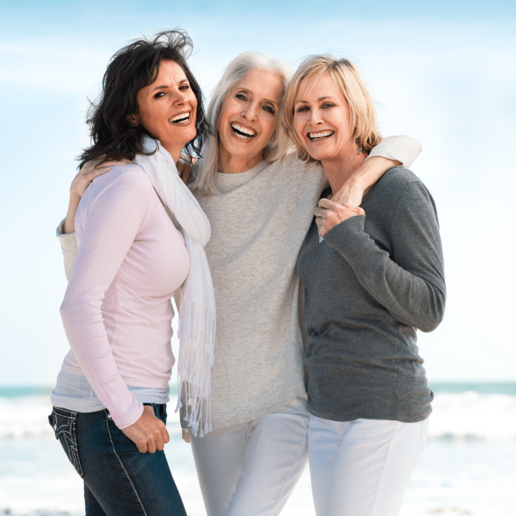 Three older women posing for a photo on the beach.