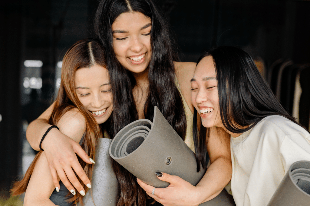 Three asian women hugging while holding yoga mats.