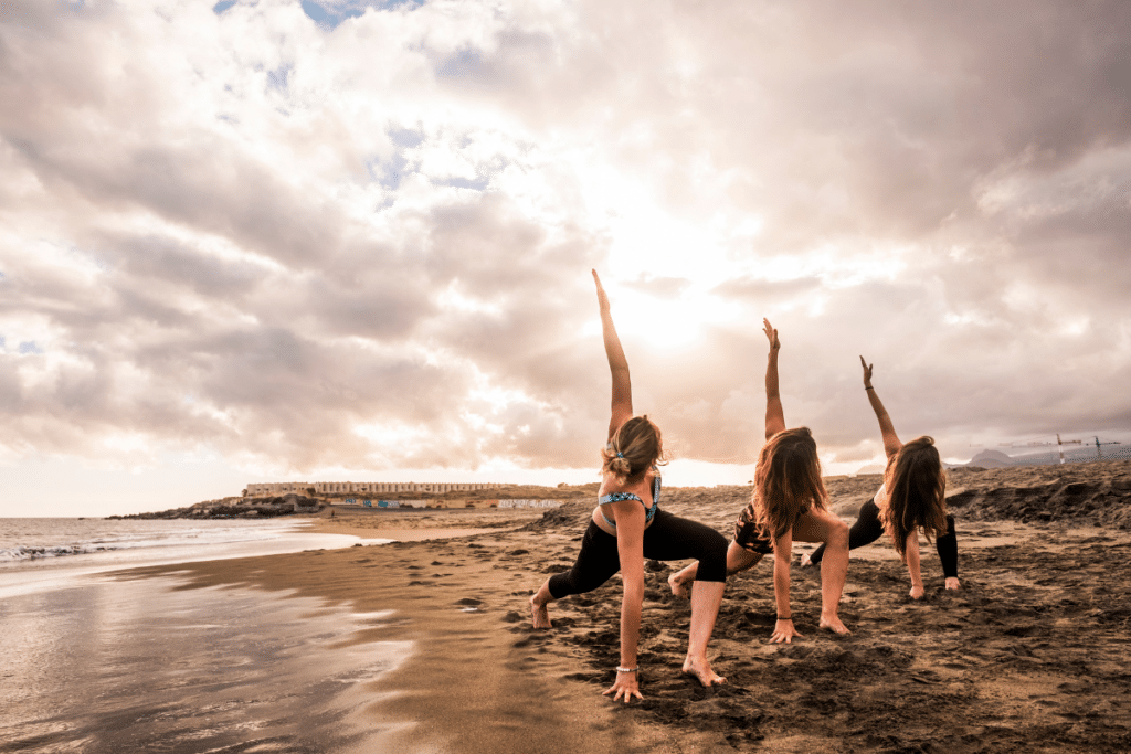 Three women doing yoga on the beach at sunset.