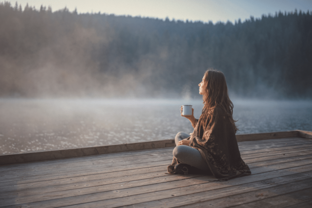 A woman sitting on a dock with a cup of coffee.