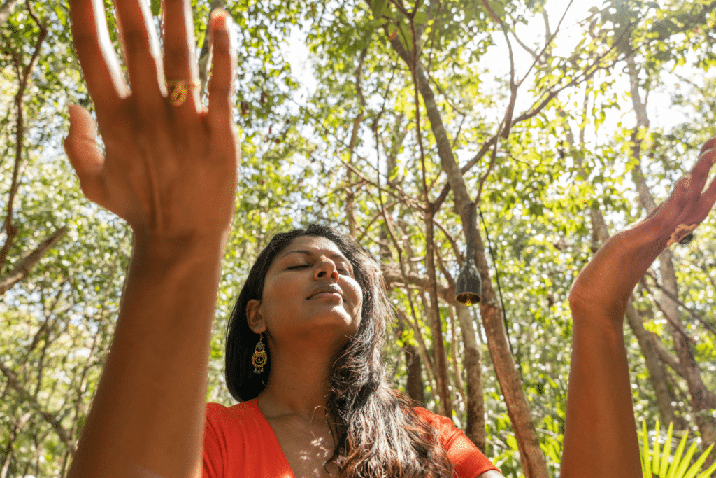 A woman with her hands up in the air in a forest.