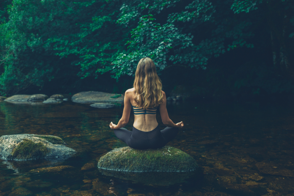 A woman is meditating on a rock in a river.
