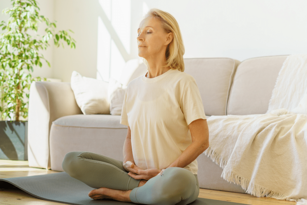 A woman is meditating on a yoga mat in front of a couch.