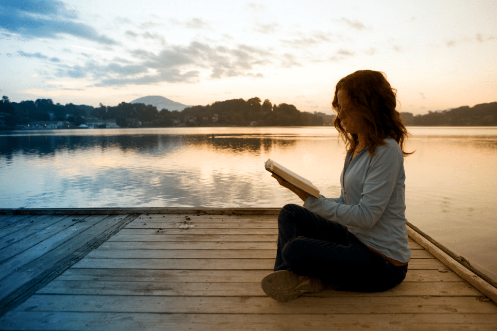 A woman sitting on a dock reading a book.