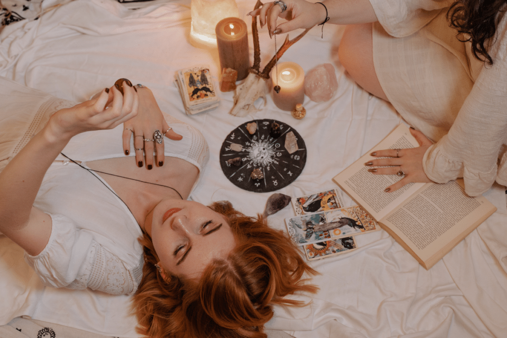 Two women laying on a bed with candles and tarot cards.