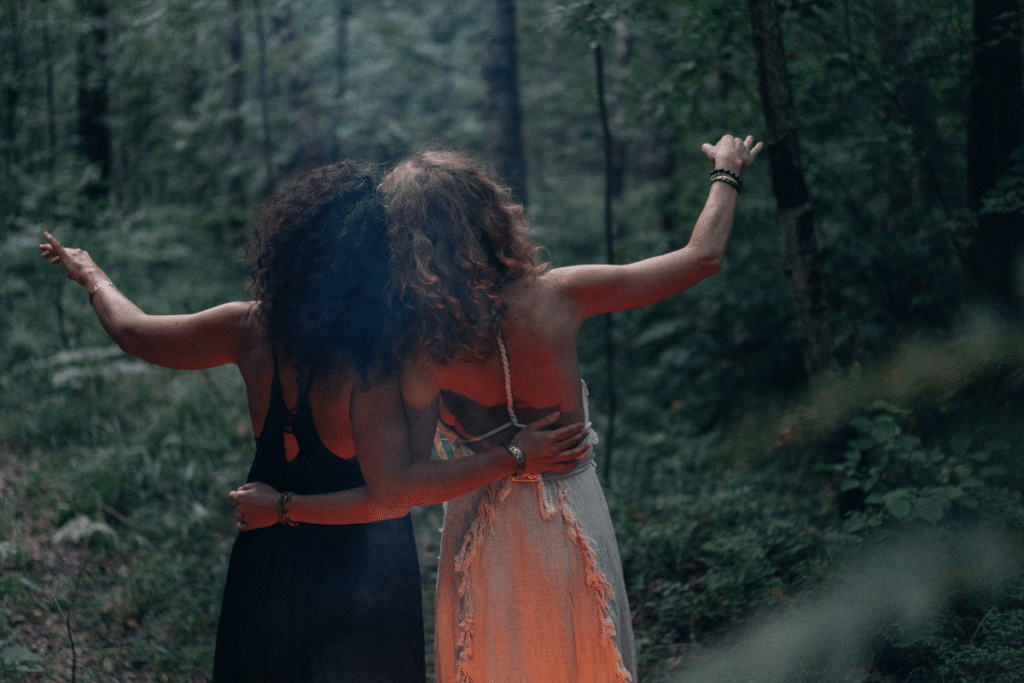 Two women standing in the woods with their arms outstretched.
