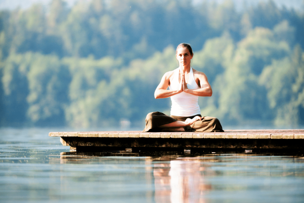 A woman meditating on a dock in a lake.