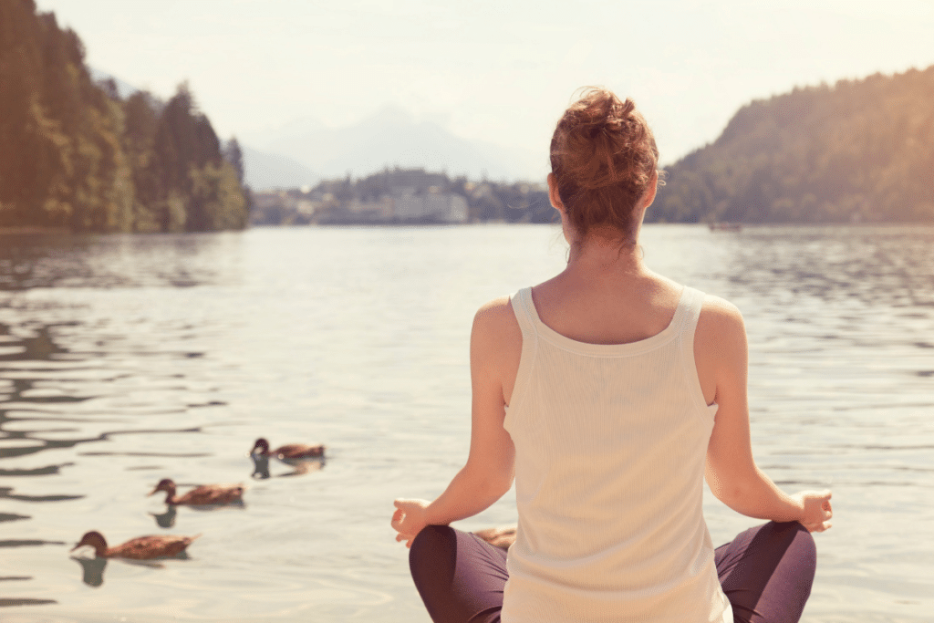 A woman is meditating in front of a lake.